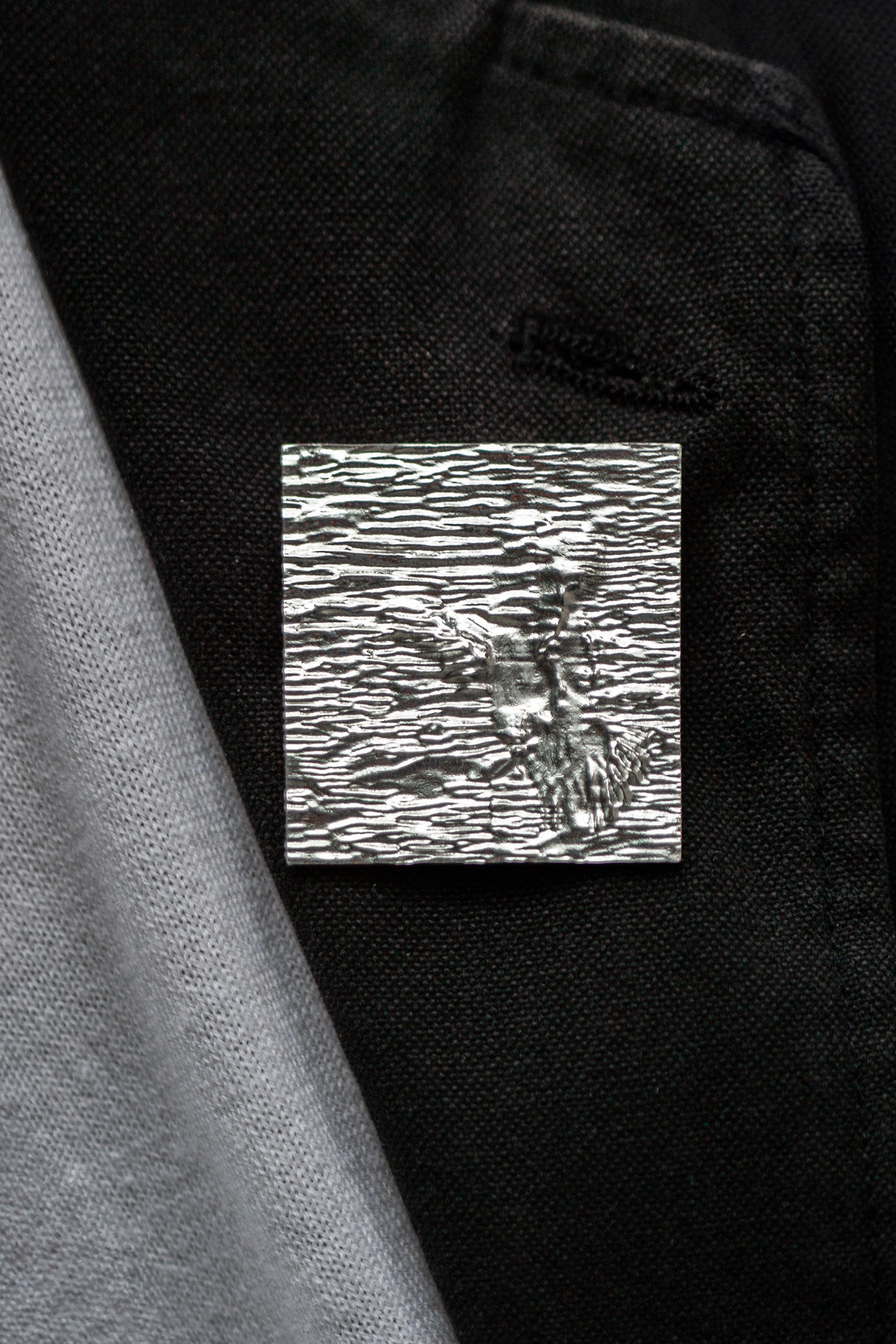 Black jacket collar with a textured square silver brooch on the lapel